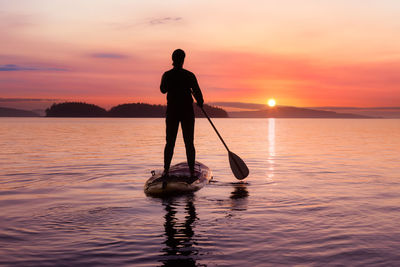 Silhouette man standing in sea against sky during sunset