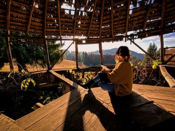 Midsection of woman sitting on wood against tree