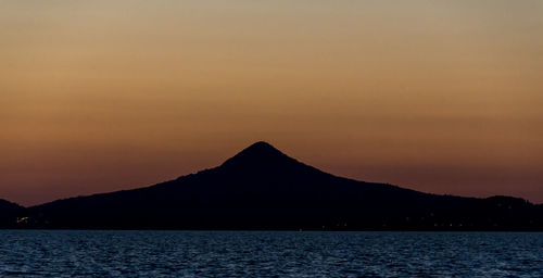 Silhouette mountain by sea against clear sky during sunset