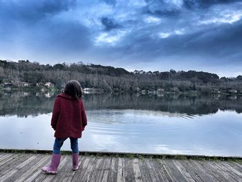 Rear view of woman standing by lake against sky