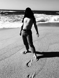 Full length of man covering face with shirt while standing at beach