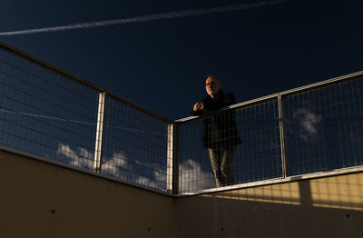 Adult man standing against fence with blue cloudy sky during sunset