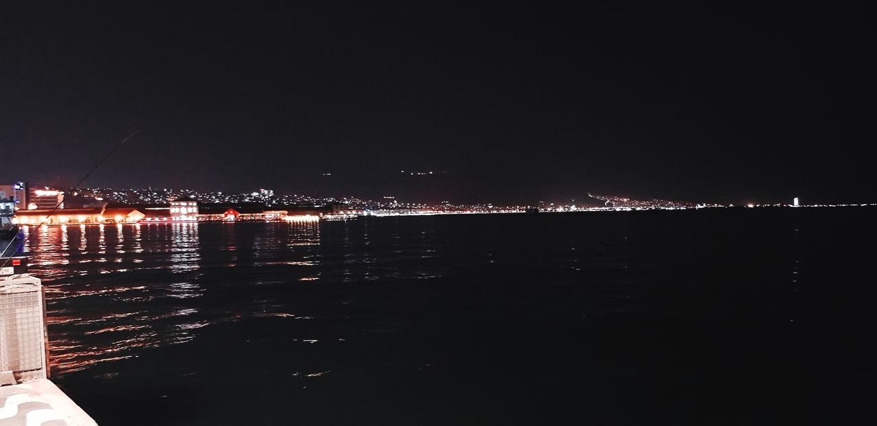 ILLUMINATED CITY BY SEA AGAINST SKY AT NIGHT