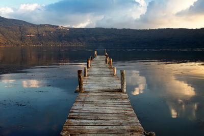 Wooden jetty over lake by mountains against cloudy sky