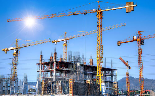 Low angle view of cranes against blue sky