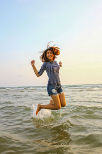 Full length of happy woman jumping in sea against sky