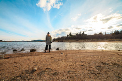 Rear view of woman standing on shore at beach against sky