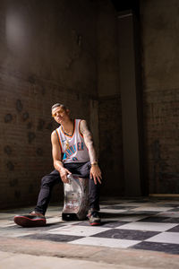 Full length portrait of young man sitting against wall