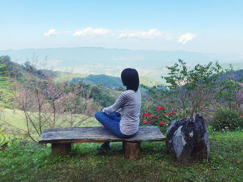 Rear view of woman sitting on plants against sky