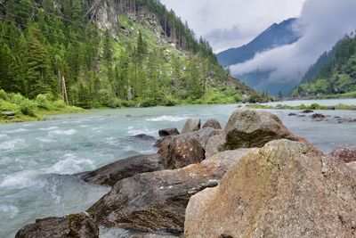 Scenic view of rocks by river in the mountains against foggy sky