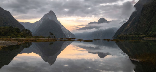Sunrise in fjord with peaks shrouded in clouds and reflection on water surface. milford sound, new z
