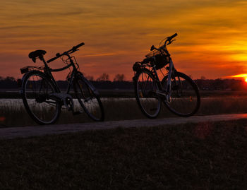 Bicycles parked on field against orange sky during sunset