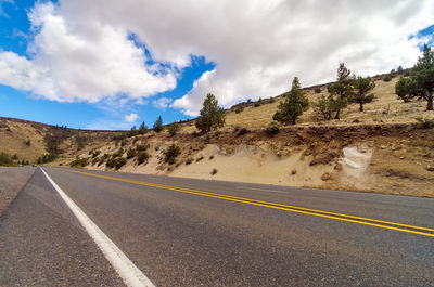 Empty country road against cloudy sky