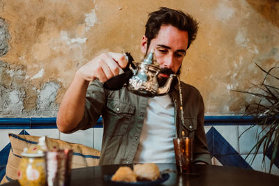 Man pouring drink in glass on table while sitting in restaurant