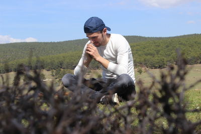 Young man sitting on land against sky