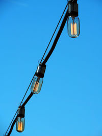 Low angle view of light bulbs against clear blue sky