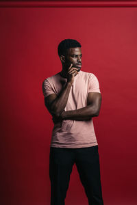 Portrait of young man looking away against red background