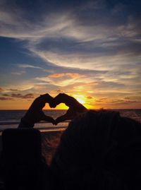 Close-up of silhouette hand on heart shape against sky