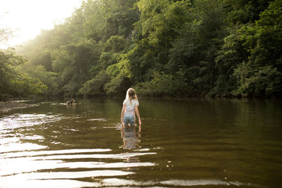 Rear view of girl wading in lake at forest