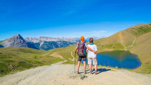 Rear view of people standing on mountain against blue sky