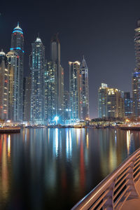 Illuminated buildings by river against sky at night