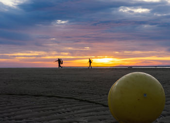Silhouette people standing on beach against sky during sunset