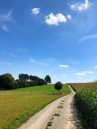 Empty road amidst field against sky