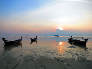 Boats moored on sea against sky during sunset