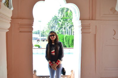 Portrait of woman in sunglasses standing against window