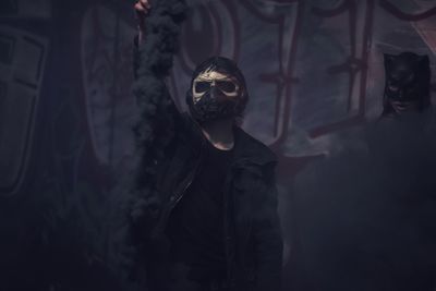 Man in mask holding distress flare while standing against wall