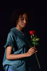 Beautiful woman holding red rose against black background