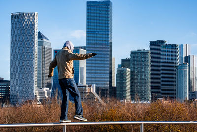 Rear view of man standing against modern buildings in city