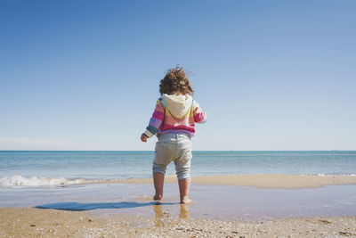 Rear view of woman standing at beach against clear sky