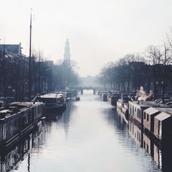 Canal in city against sky during foggy weather