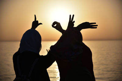 Silhouette friends gesturing against sea during sunset