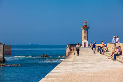 People on lighthouse by sea against clear blue sky