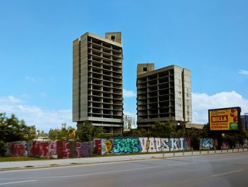 Road by buildings against blue sky