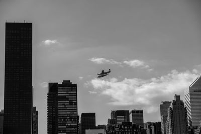 Low angle view of silhouette airplane flying over cityscape against sky