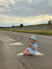 Portrait of boy sitting on road against sky