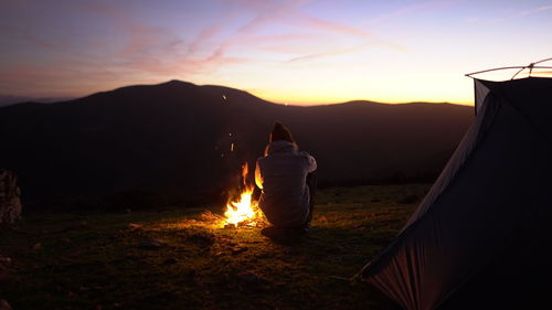 Man enjoys a campfire with sunset view next to a tent