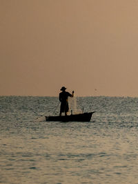 Silhouette man on boat in sea against sky during sunset