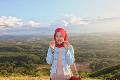 Smiling woman wearing sunglasses with landscape in background against sky