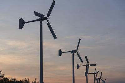 Low angle view of wind turbines against sky during sunset