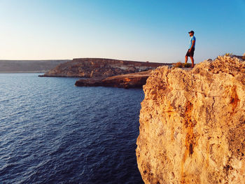 Man standing on cliffs by sea against sky