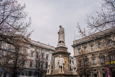 Low angle view of statue by building against sky