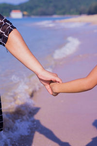 Midsection of people holding hands on sea 