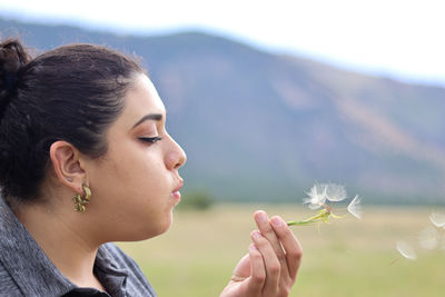 Portrait of young woman holding dandelion against white background