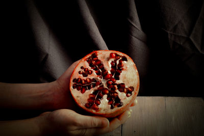 Close-up of hand holding pomegranate over black background