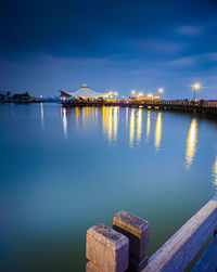 Illuminated wooden posts in sea against blue sky