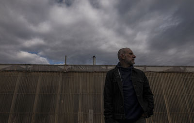 Adult man standing in front of plastic greenhouses against cloudy sky in almeria, spain